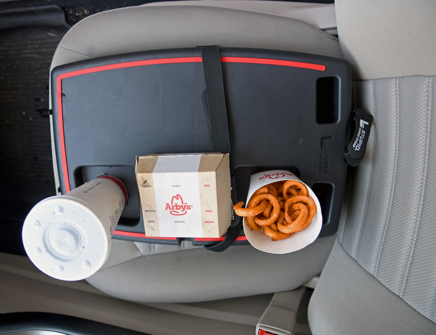 The Stupid car tray organizer inside a vehicle with food sitting on top of the tray.