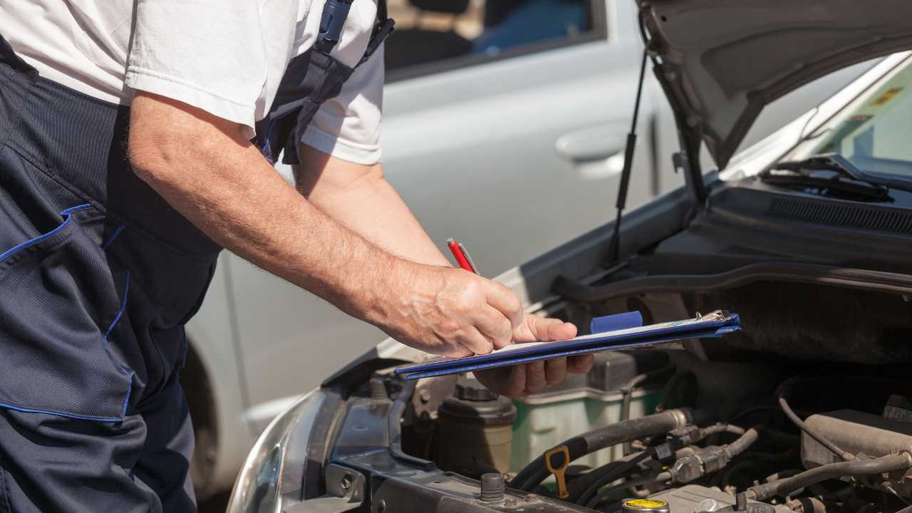 Auto mechanic checking car engine and writing on clipboard