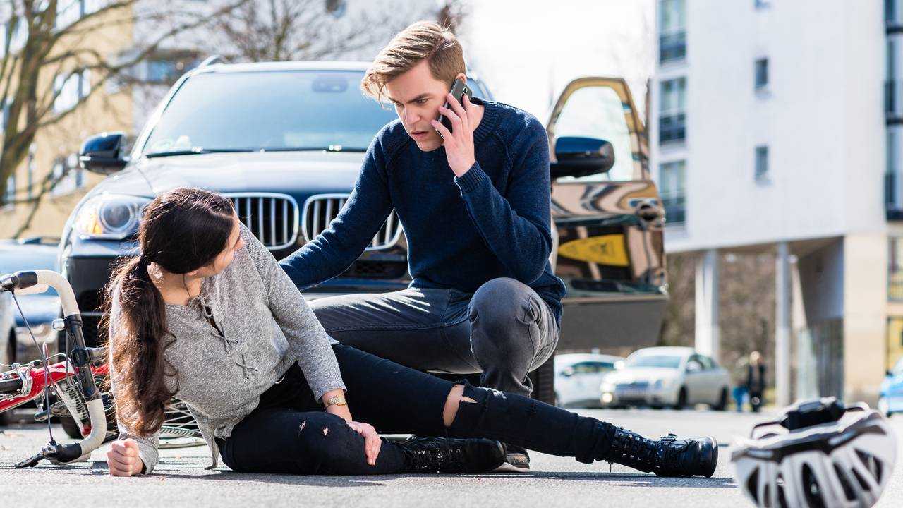 Worried young driver calling ambulance after hitting female bicyclist