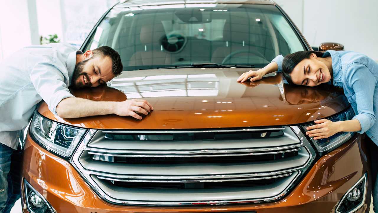 Happy young couple buying first new family car together in dealership
