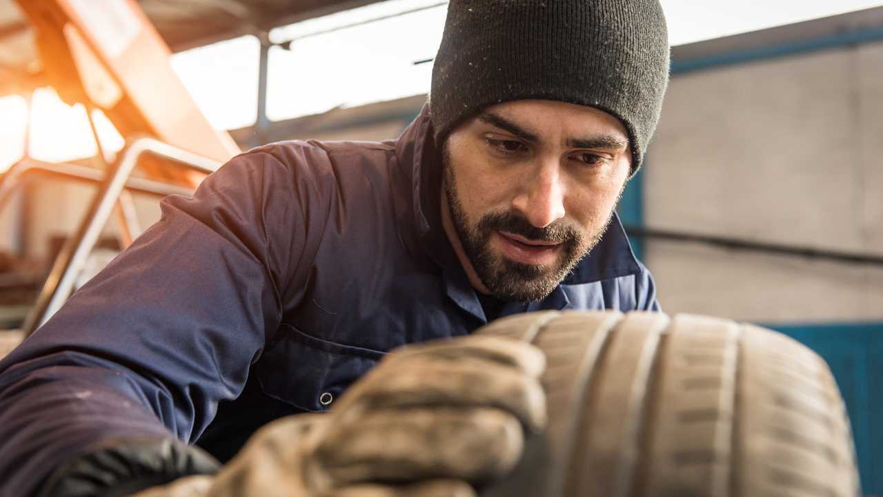 Mechanic checking depth of tyre tread for wear
