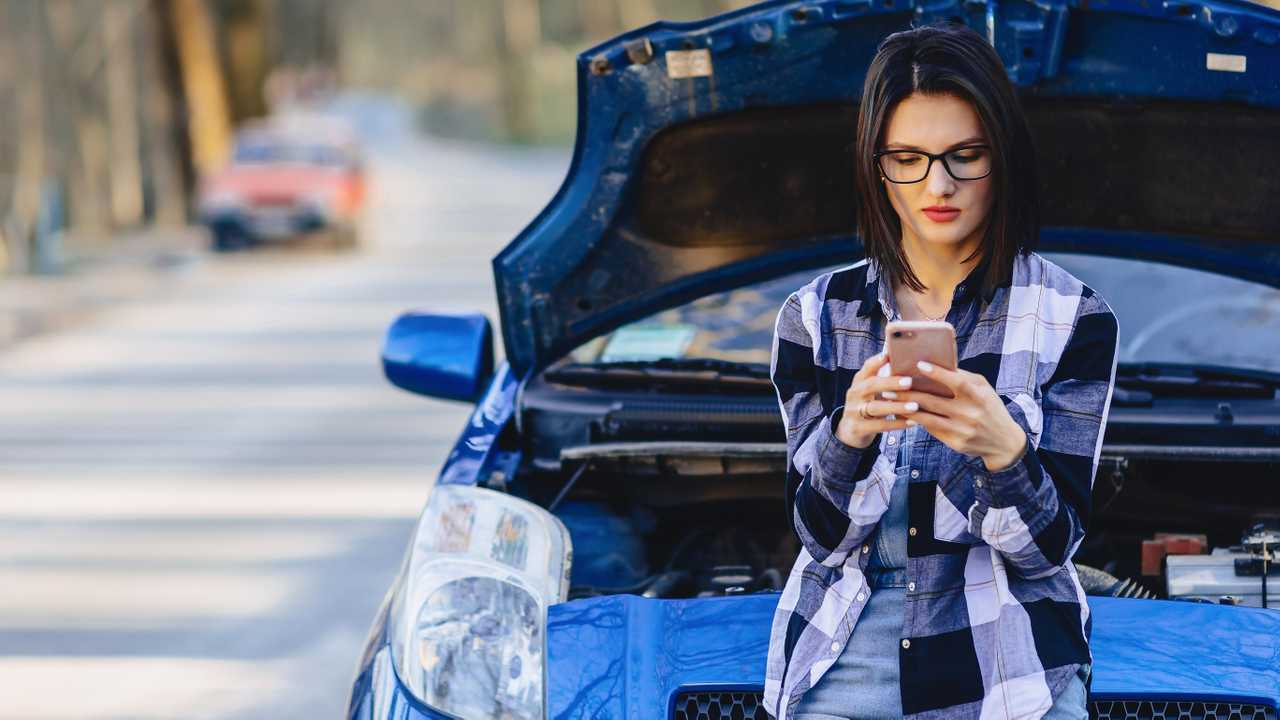 Woman with phone with broken down car on road