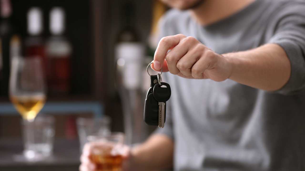 Man holding car key and alcoholic beverage