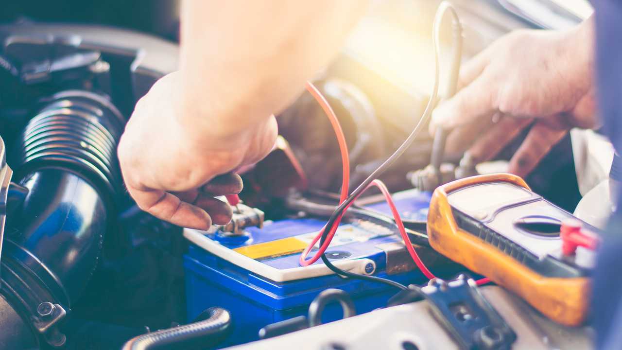 Mechanic uses multimeter on car battery