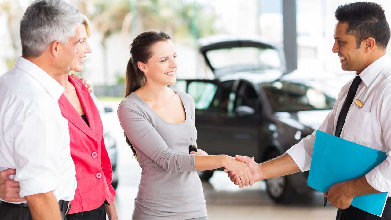 Car salesman shaking hands with young adult customer with parents