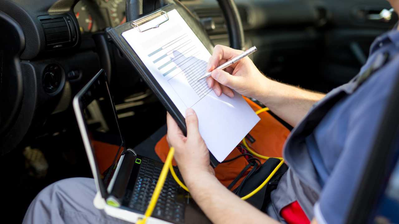 Mechanic writing on clipboard sitting in car being serviced