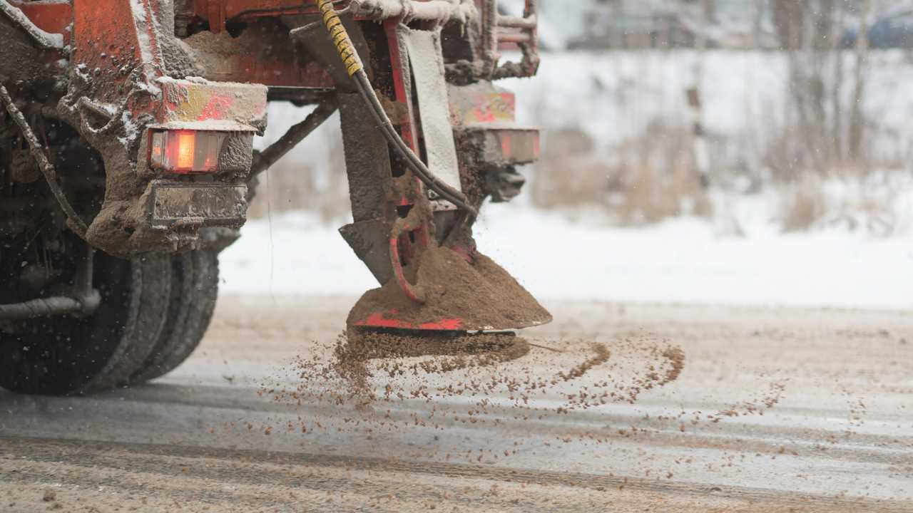 Highway maintenance truck spreading salt and sand on road
