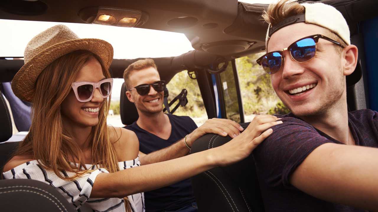 Group of friends driving open top car without seatbelts