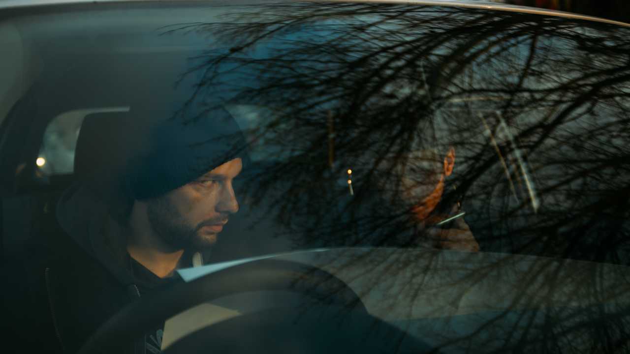 Thieves sitting in a car talking on the phone and planning their next target