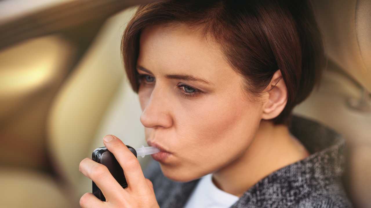 Woman using breath alcohol breathalyser in the car