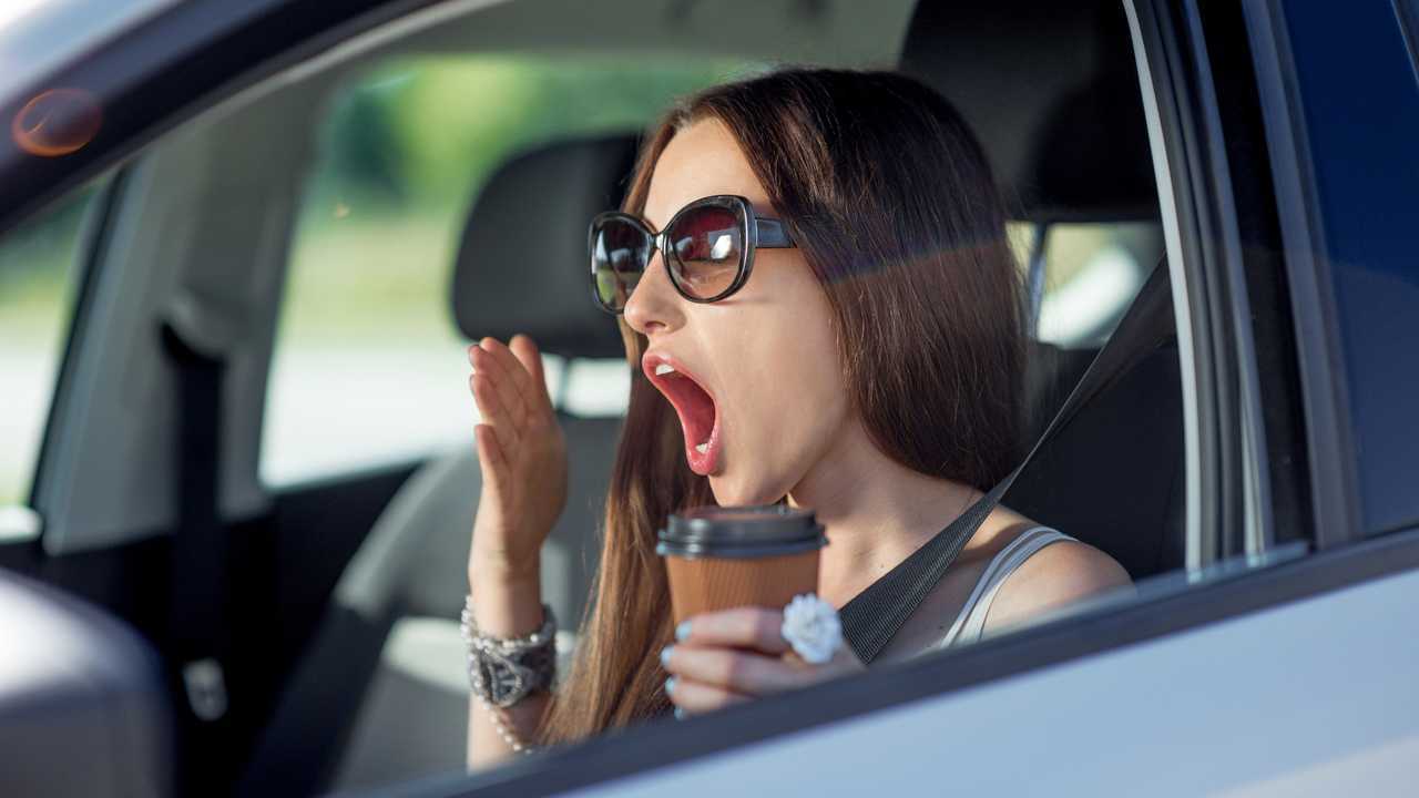 Young woman yawning with cup of coffee in her car