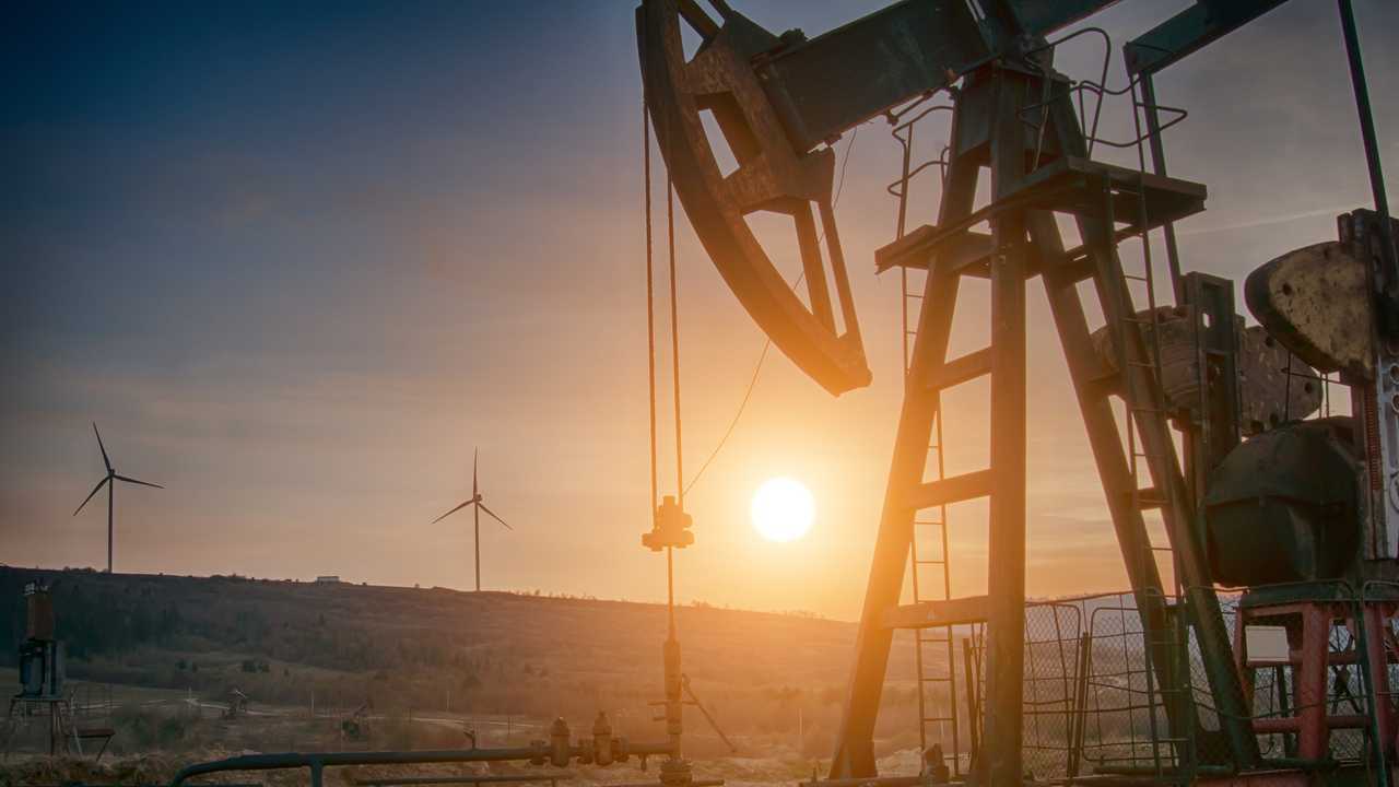 Oil pump at sunset with wind mills in background