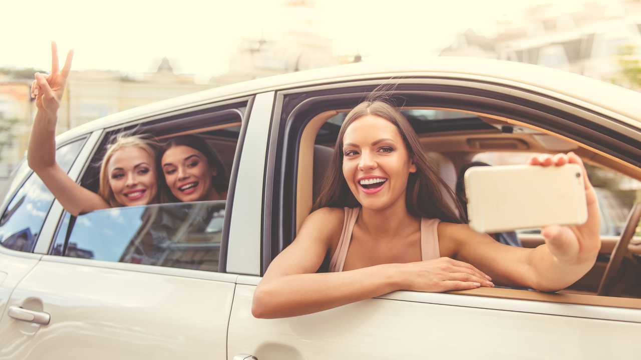 Young women taking selfies with phone while leaning out car window
