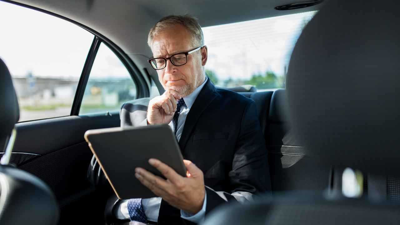 Businessman with tablet computer riding in car back seat