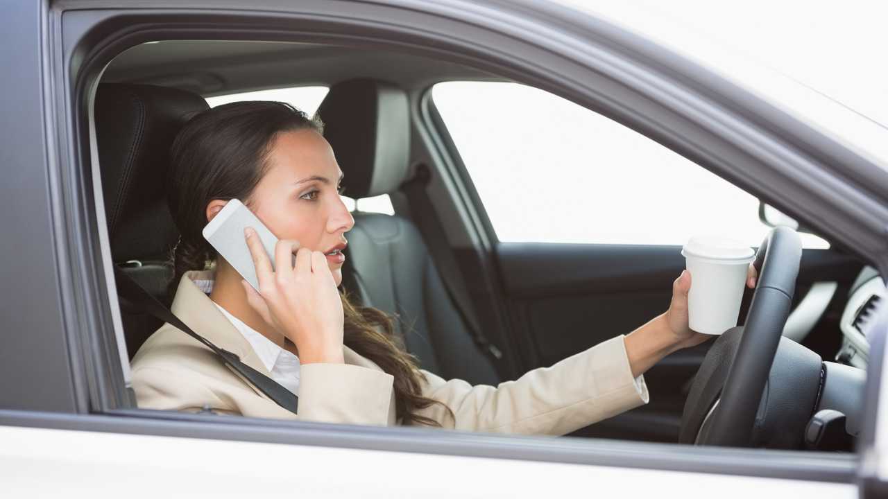 Woman drinking coffee on phone while driving in car