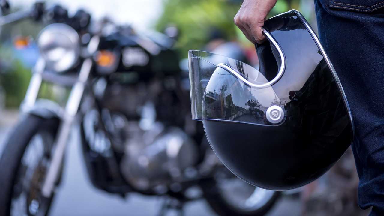 Man holding helmet and vintage motorcycle in background