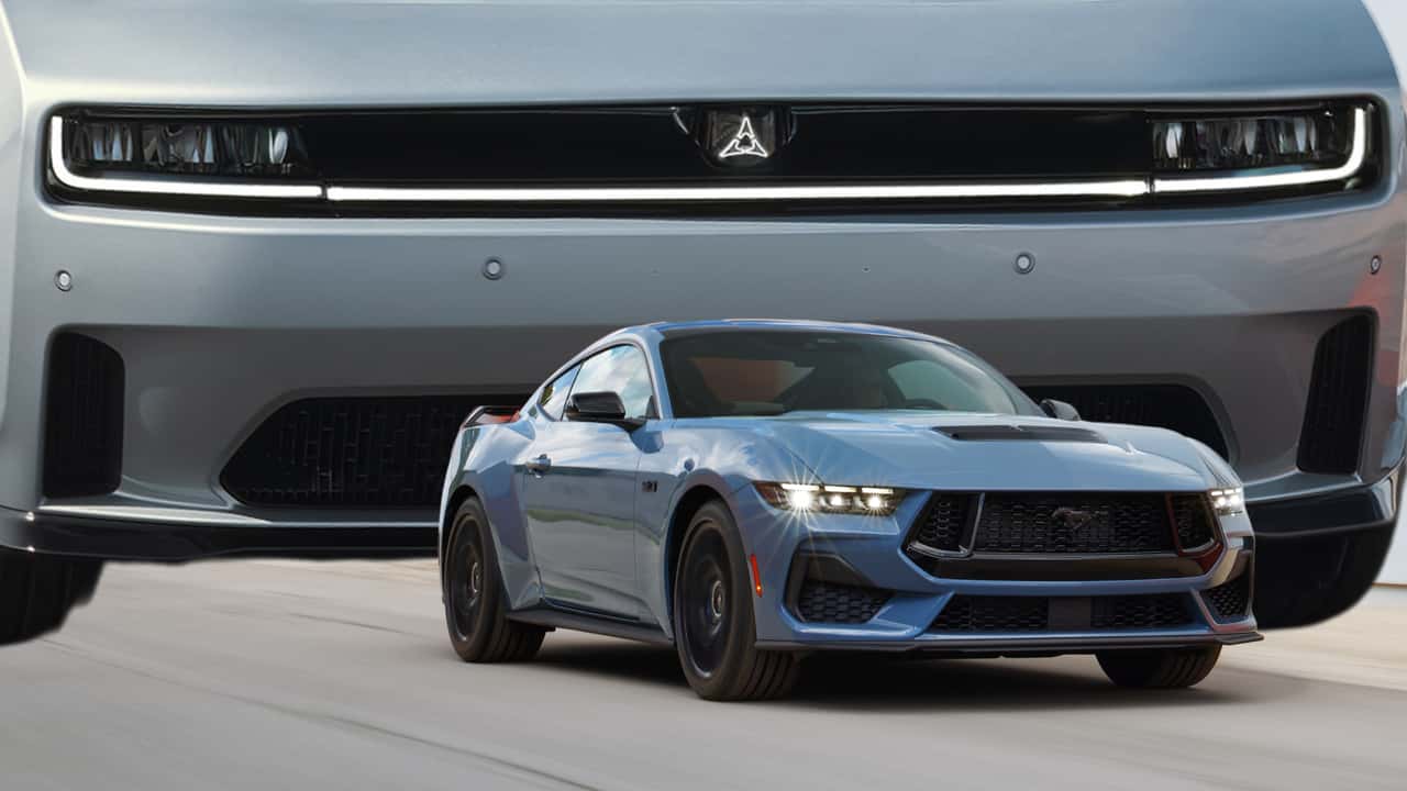 ford mustang driving on a road while a clownishly large charger looms in the background