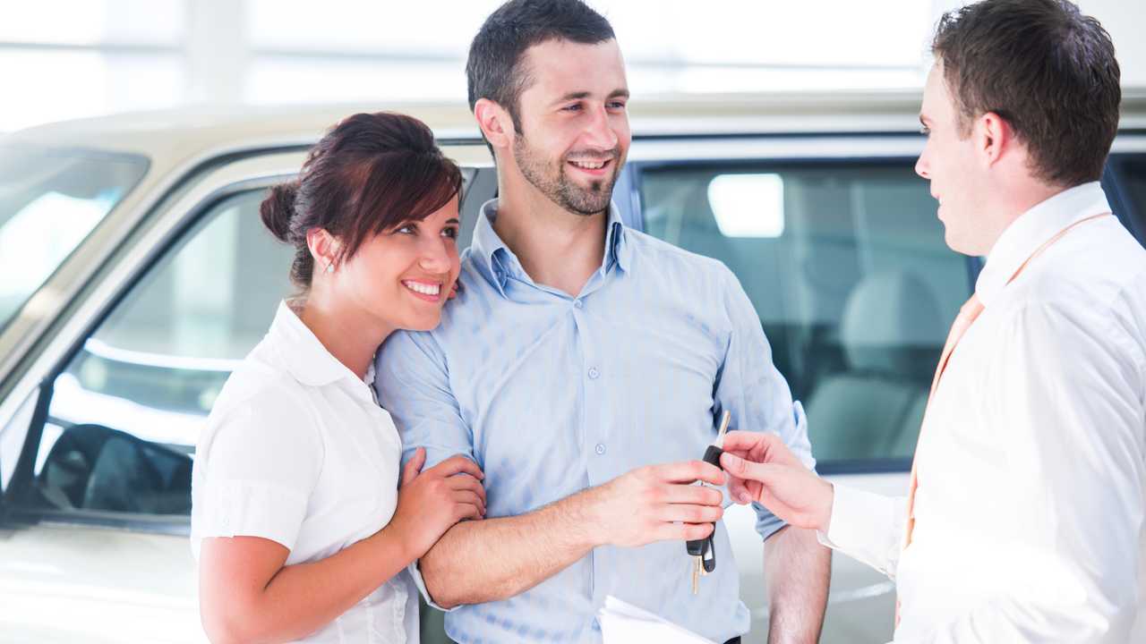 Smiling couple buying a new car from a salesman