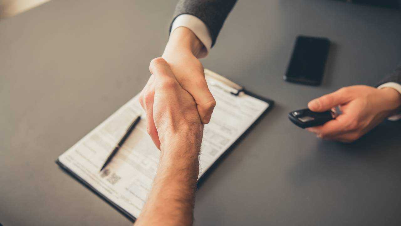 Men shaking hands while signing documents at car dealership