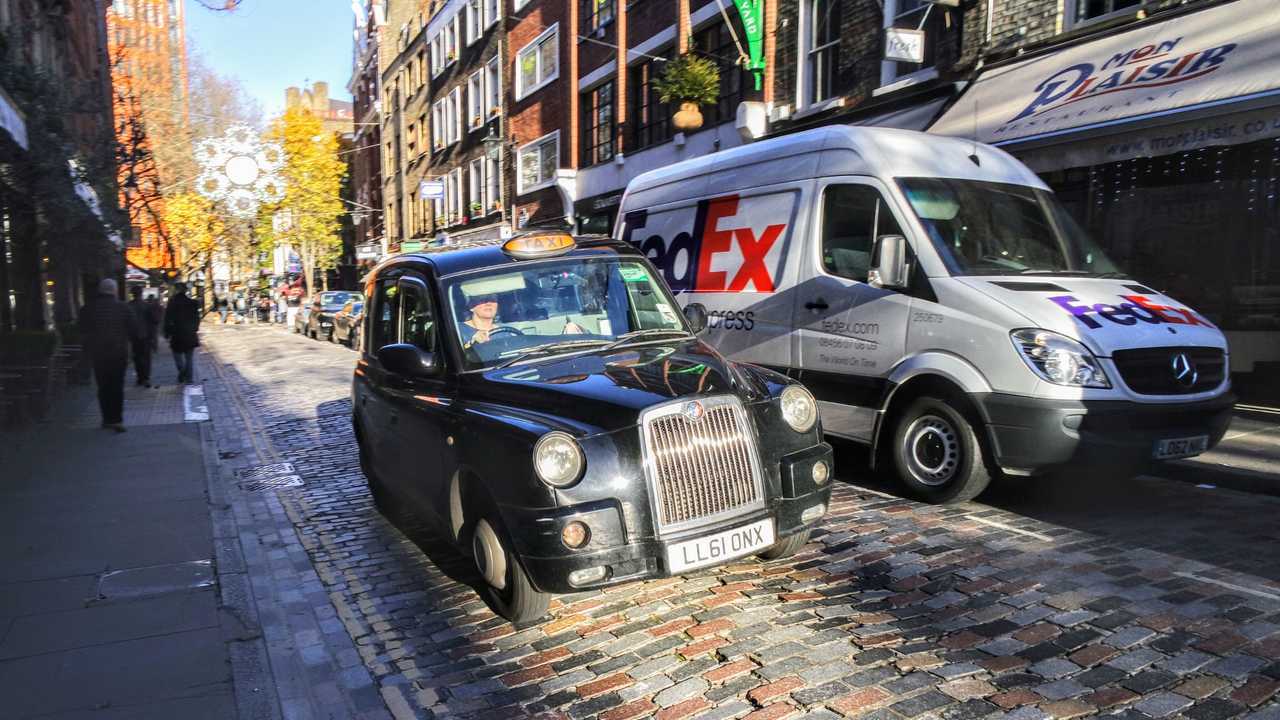 Taxi with FedEx van on brick road in London