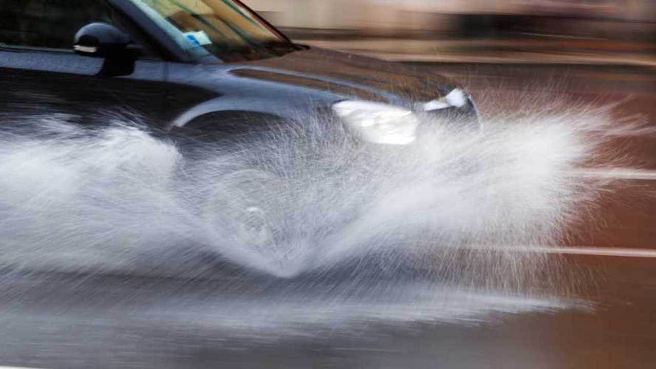 Car drives through puddle splashing rain water
