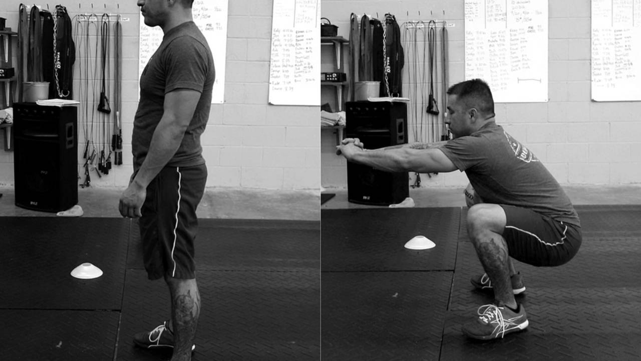 Gino shows us an air squat. His arms are out in front of him for balance. If you squat with a heavy implement, hold it close to your chest.