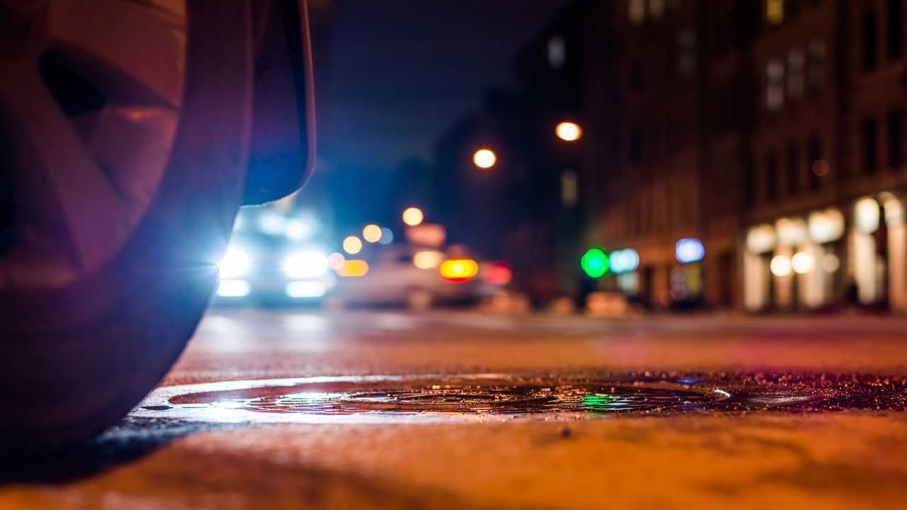 Car wheel around manhole on city street at night