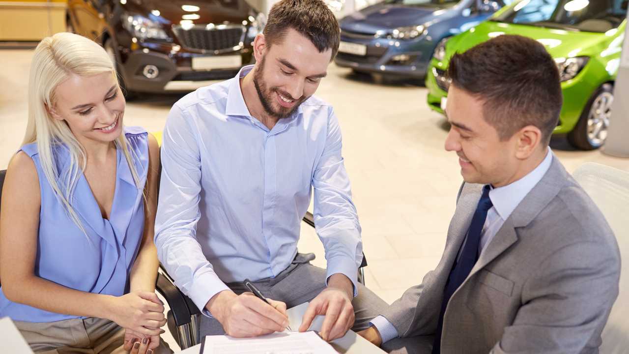 Couple with dealer buying car and signing documents