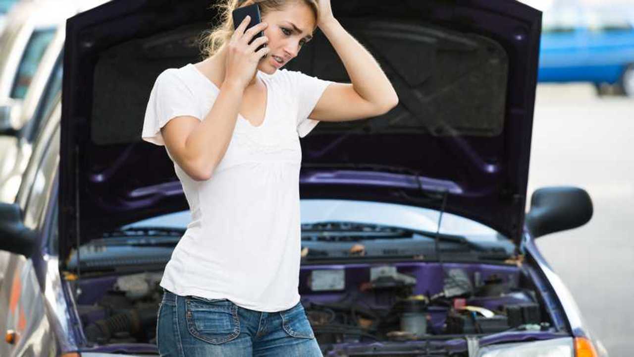 Woman using phone while looking at broken down car