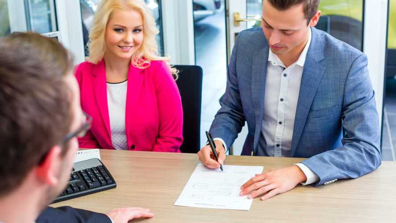 Couple buying car at dealership and signing sales contract with salesman