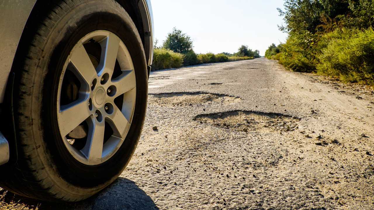 Car wheel on damaged road with big potholes