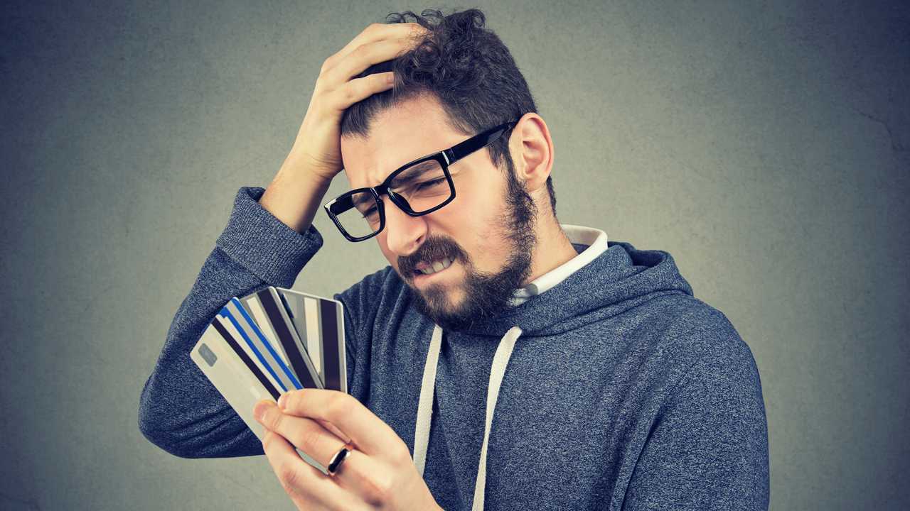 Confused stressed man looking at too many credit cards full of debt